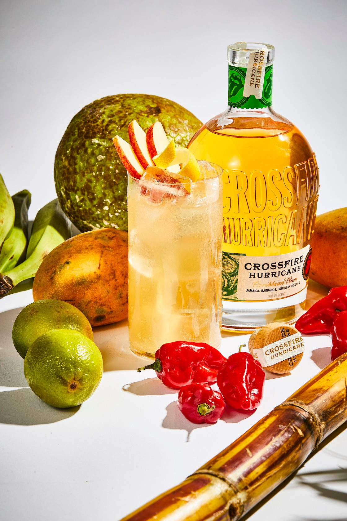 Crossfire Hurricane Rum next to a cocktail on a table full of fruit.